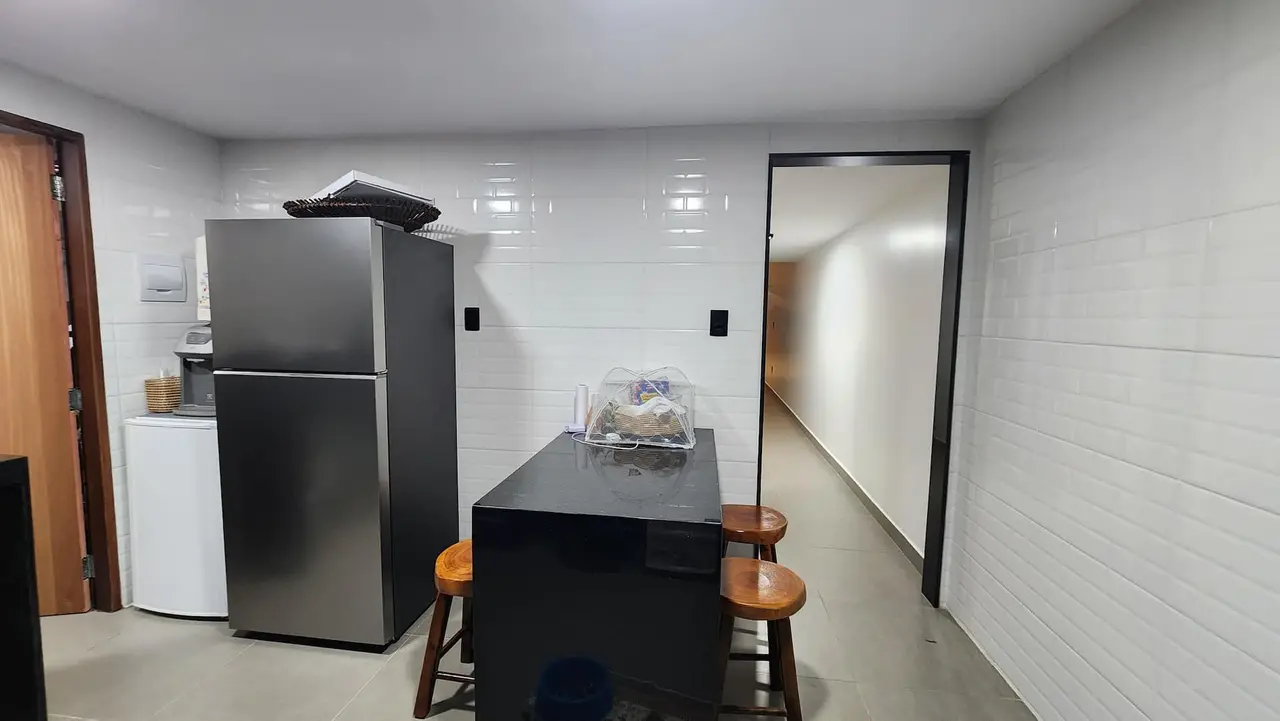 Cozinha com geladeira inox, frigobar e bancada com bancos de madeira