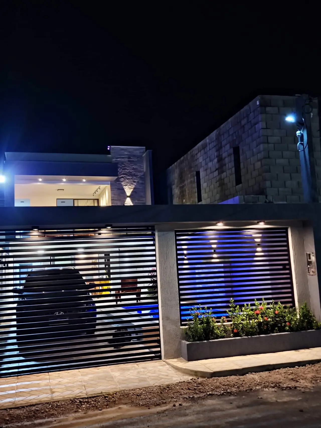 Fachada da casa à noite, com portão de ripas e iluminação