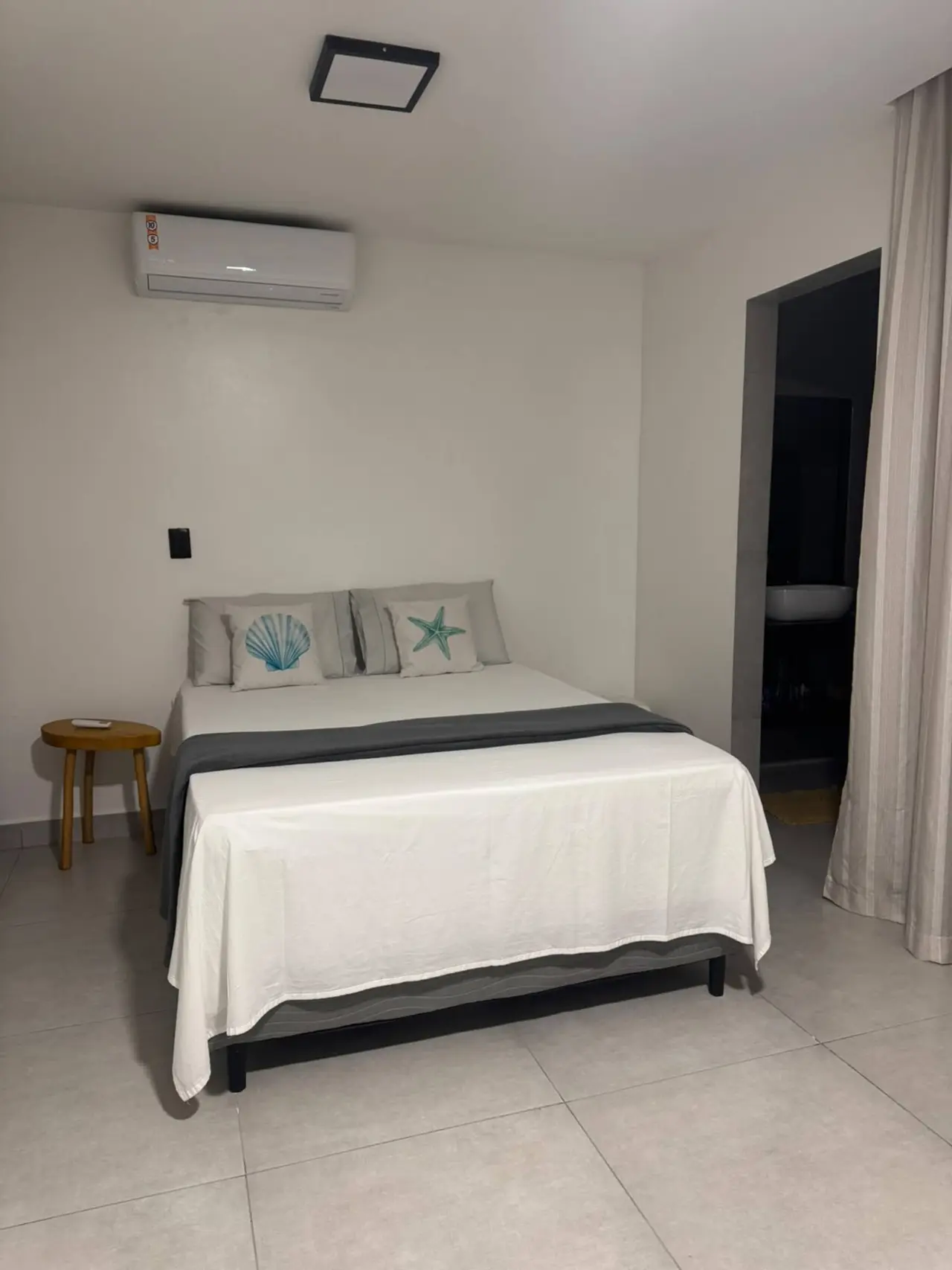 Quarto com cama de casal, ar-condicionado e banheiro ao fundo
