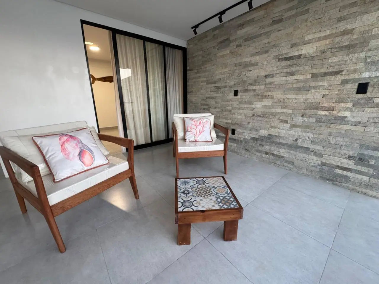 Poltronas de madeira e mesa com azulejos em frente a uma parede de pedra