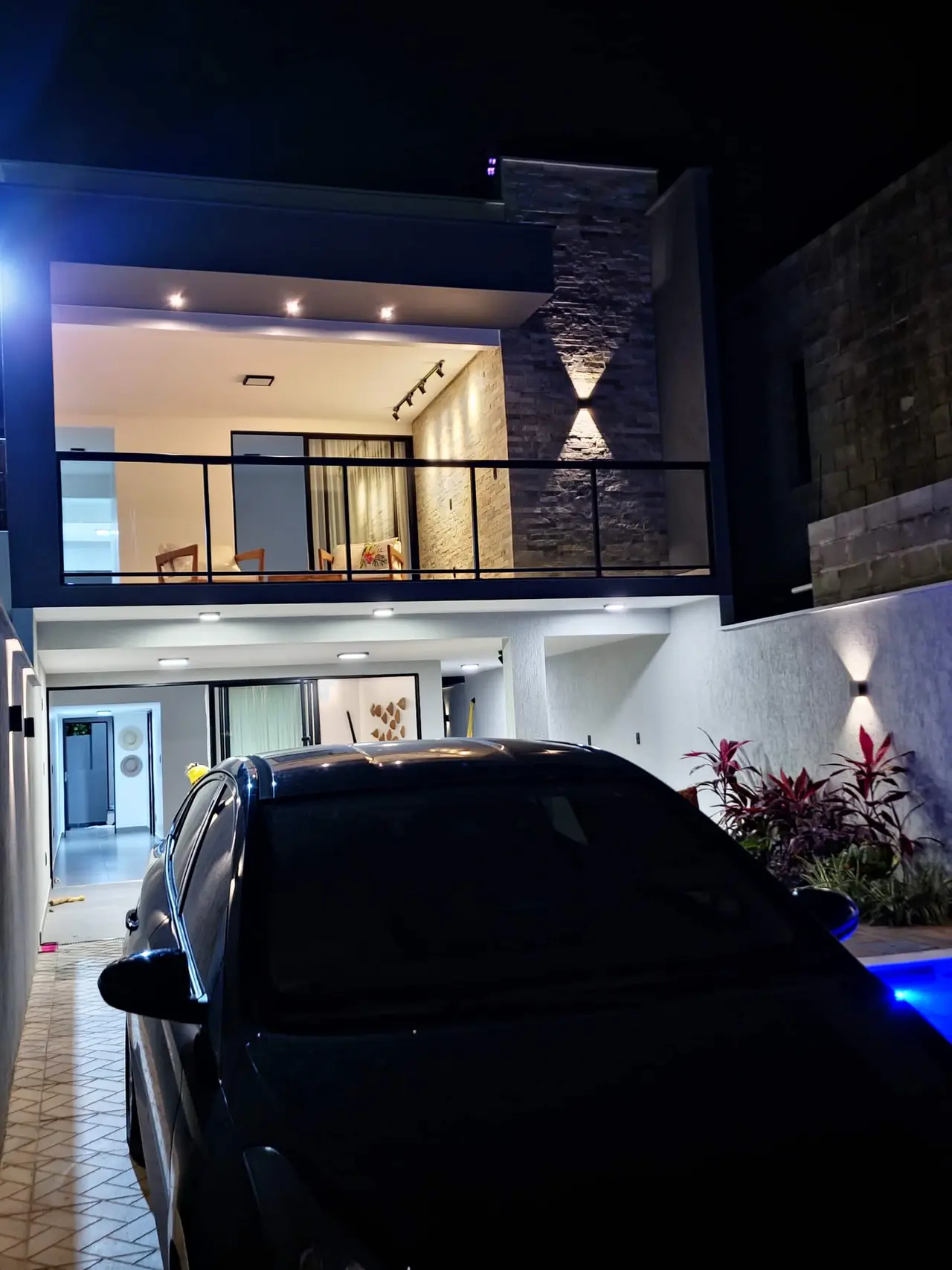 Fachada de dois andares à noite, com sacada e o brilho da piscina
