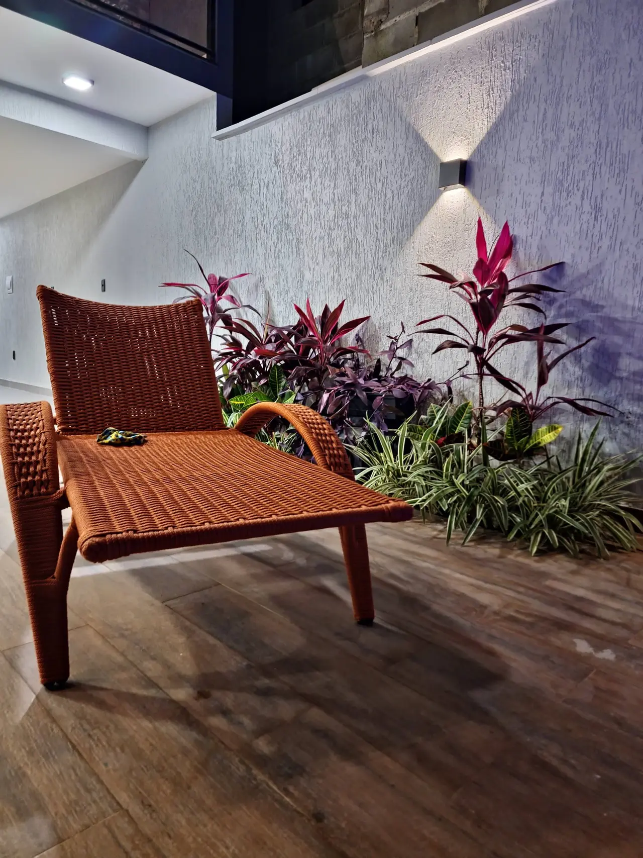 Espreguiçadeira de palhinha entre plantas ao lado da piscina